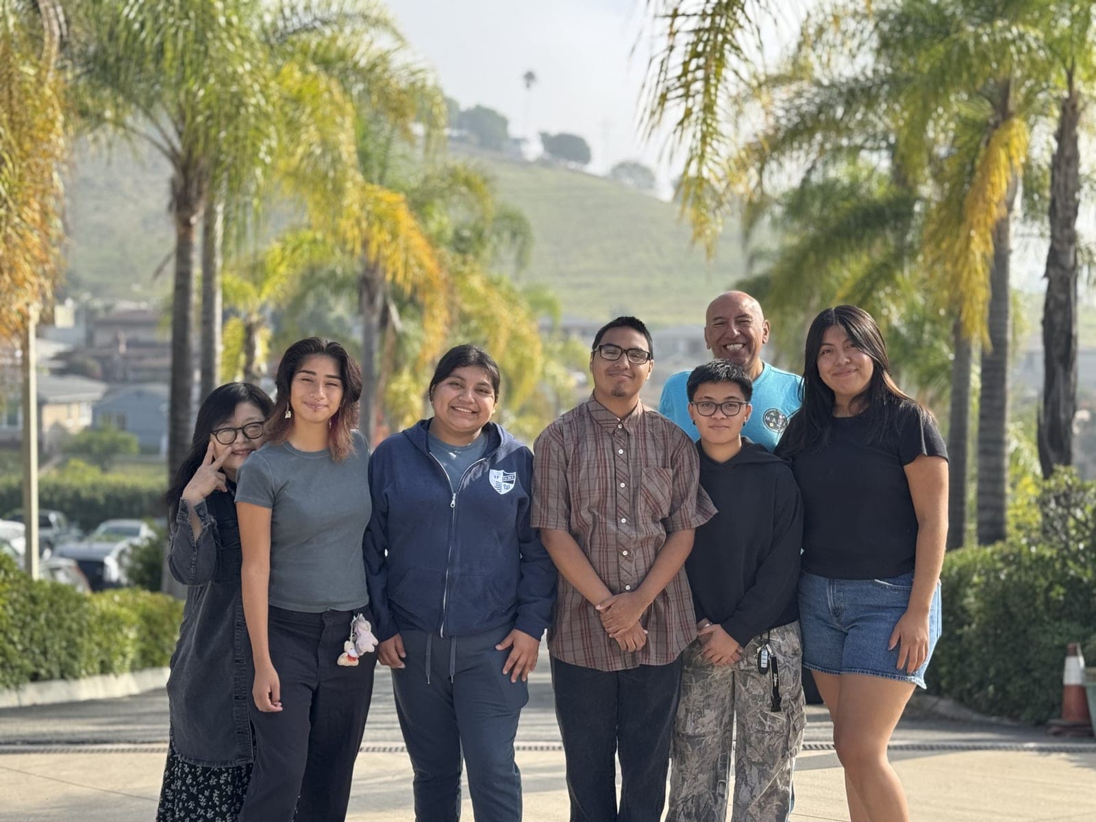 A group of MFC mentors, mentees, and staff smiling together among palm trees