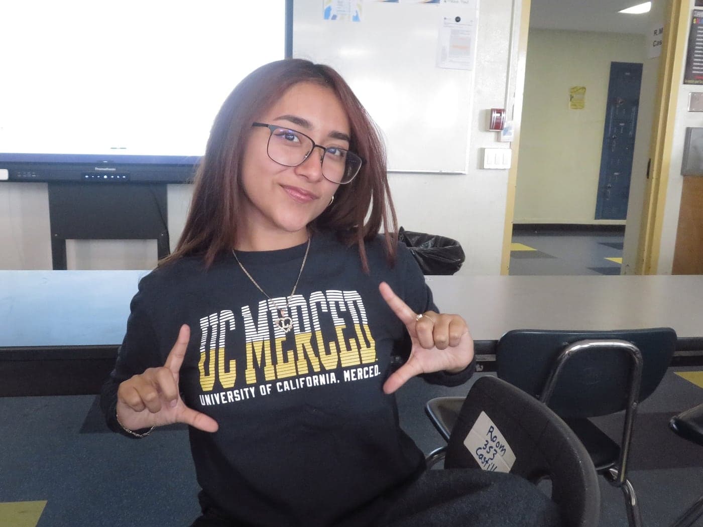 A mentee in a UC Merced sweatshirt making a hand sign