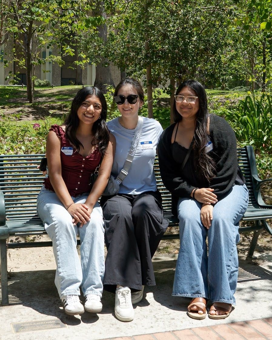 Three young women sitting together on a bench outdoors