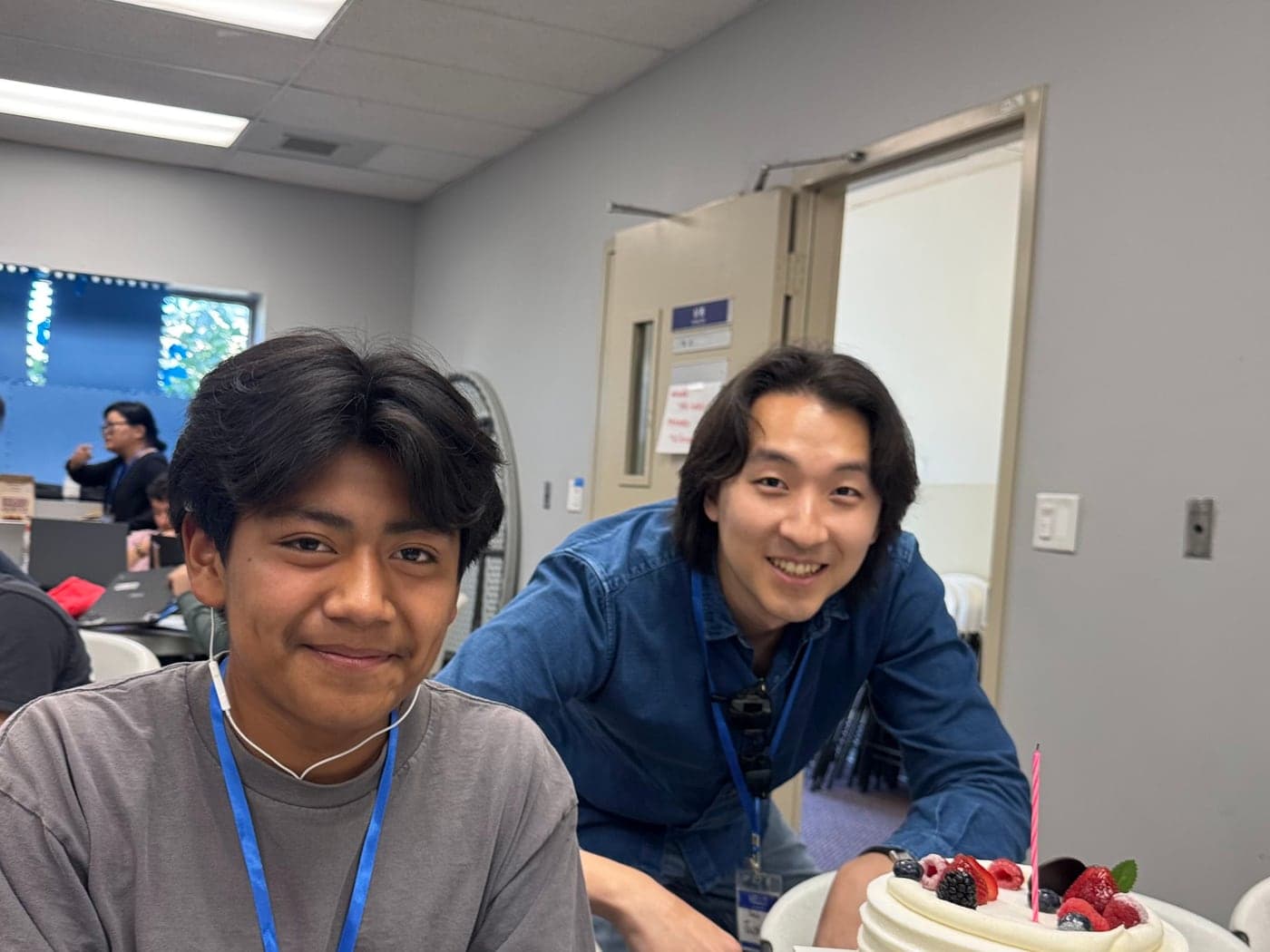 A young person and an older mentor smiling together next to a birthday cake